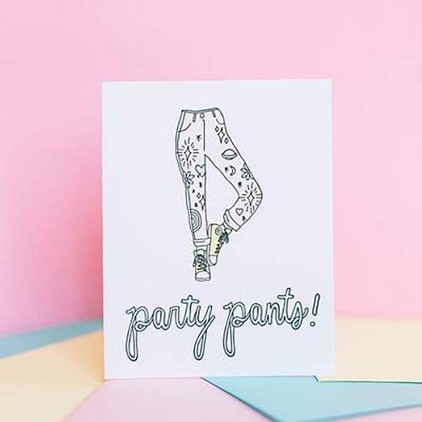A white greeting card with black outlined pants decorated with various fun symbols and the text "party pants!" below it. The background is light pink, yellow and mint.