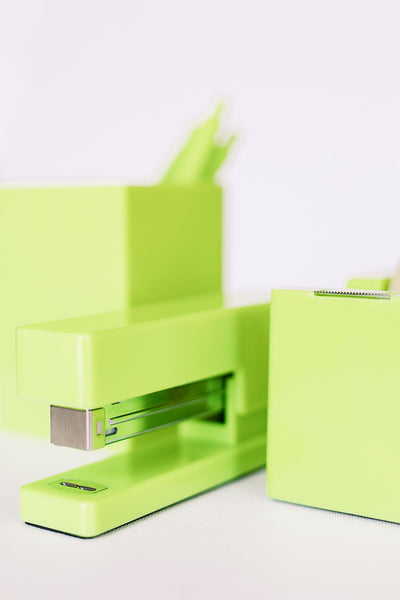 Lifetsyle photo of a citron green stapler with a matching tape dispenser and pen cup in the background.