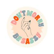 A circle-shaped sticker with a hand snapping their fingers printed on the middle of the sticker. "Don't worry, Be Sassy" printed on the perimeter in multi-colored letters surrounding the snapping fingers.