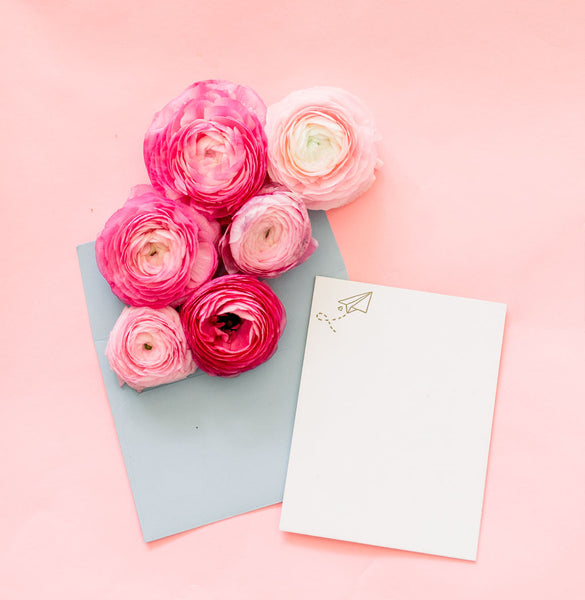A cute letter pressed card featuring a paper airplane surrounded by pink flowers.
