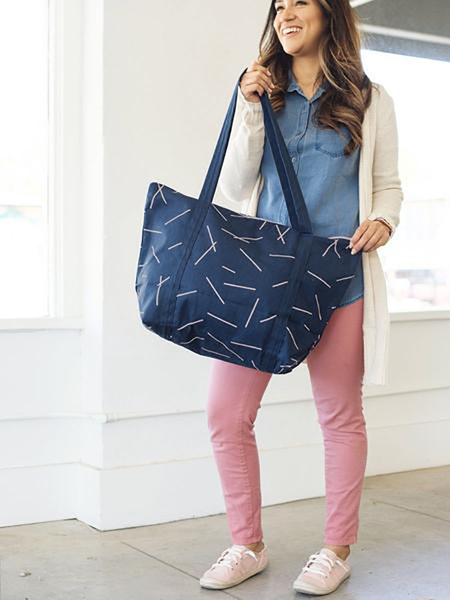 Brunette girl holding a cute tote bag in navy blue canvas with long shoulder strap and zippered top.