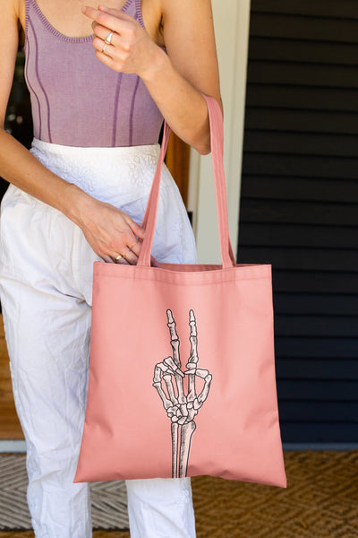 bright coral pink canvas tote bag with skeleton peace sign hand on front.