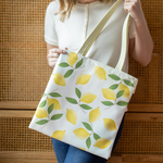 A woman holding a vegan leather tote bag printed with a pastel gradient background and lemons. 