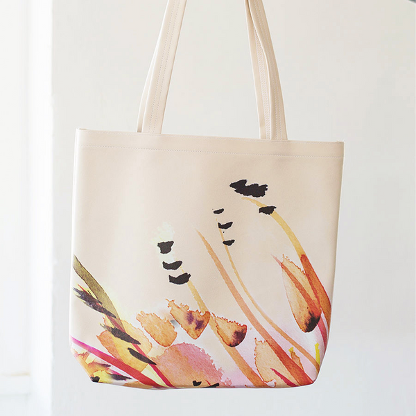 A woman's denim clad arm holding a cute tote bag in peach with large tropical flower.