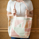 Woman's hand holding a cute tote bag with geometric fruit design and peach shoulder straps