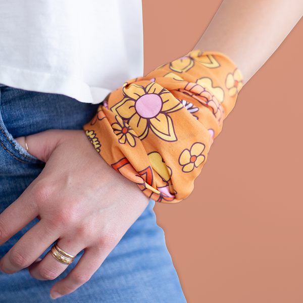 An orange mask-like item with multicolored and differently designed, wrapped around a person's wrist. 