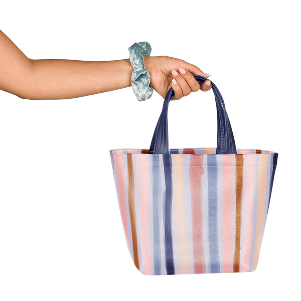 Girl with scrunchie on wrist holding a cute tote bag in purple, blue, and pink stripes pattern.