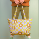 Girl holding a cool funky daisy pattern weekender. Pastel color background. 