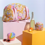 Puffy somewhere tote with floral pattern resting on colorful cubes with prosecco and sunglasses.