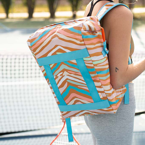 Lady with a cute tan striped cooler backpack on a tennis court.