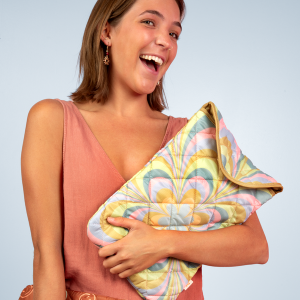 Light blue background with a girl smiling holding a puffy folder over laptop sleeve with pastel color kaleidoscope floral pattern.