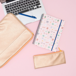 A laptop sleeve, computer, notebook and pen are sitting on a pink surface. Next to those items is a small, gold metallic pouch with an orange zipper.