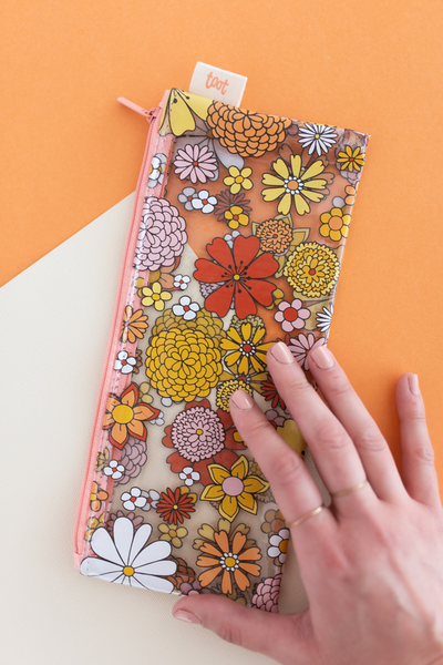 Girl hand on top of cute pencil pouch clear plastic with floral print on top with orange zippers