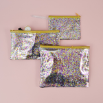 Large cosmetics pouch in clear vinyl with glitter confetti and a gold zipper.
