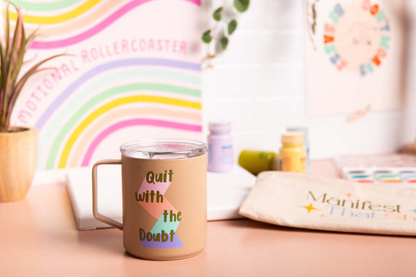 Table Setup with "Quit with the Doubt" Camp mug, "Manifest that Shit" pencil bag, and "Emotional Rollercoaster" print.