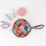 Multicolored jewel-toned floral circle pouch with zipper sitting on a white desk with lip balm nail polish and a phone charger cord.