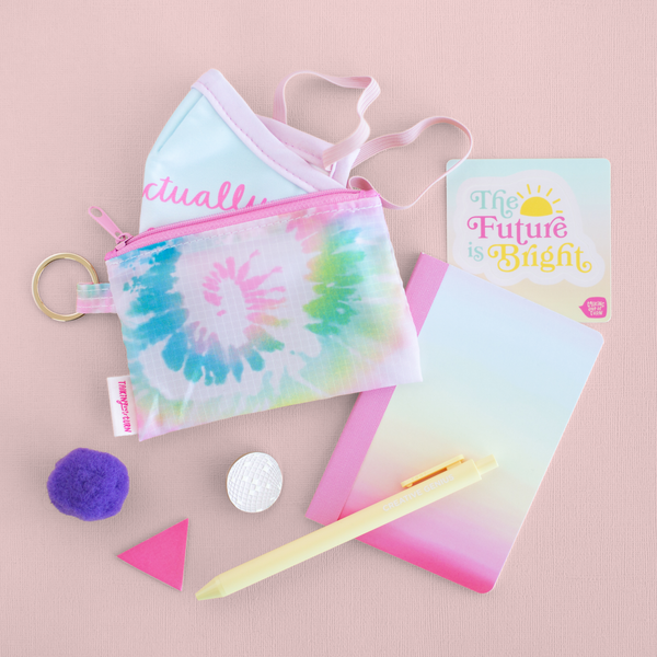 A tie dye pouch with a facemask in it next to a mini notebook and sticker that says the future is bright