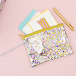 Small pouch wristlet in clear vinyl with glitter confetti, gold zipper, and vinyl strap.