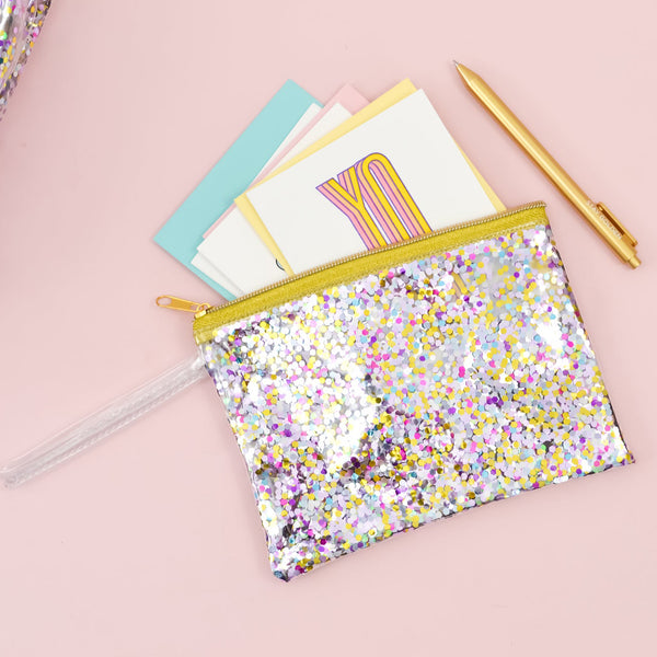 Small pouch wristlet in clear vinyl with glitter confetti, gold zipper, and vinyl strap.
