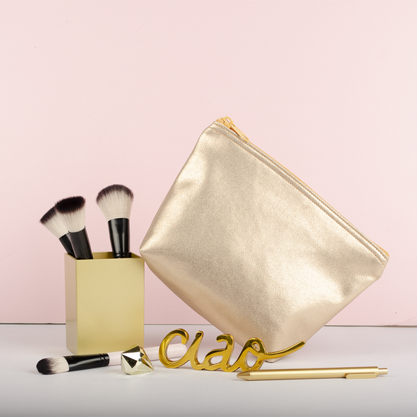 A cute makeup bag sits with a gold makeup brush holder and ciao sculpture.
