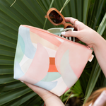 A medium sized pouch with overlapping moon phases printed on in different pastel colors. Being held by a person in front of a plant.