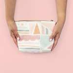 Two hands holding a cute cosmetics bag with a muted geometric print.