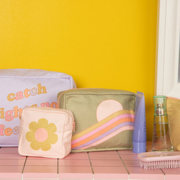Mustard yellow background with three waffle pouches on a pink squared surface along with misc items. 