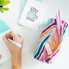 A wild-striped multicolored Ladybug pouch with two Jotters, washi tape, and other stationary displayed inside. A 