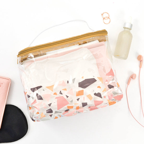A cute toiletries bag in a terrazzo pattern surrounded by toiletries.
