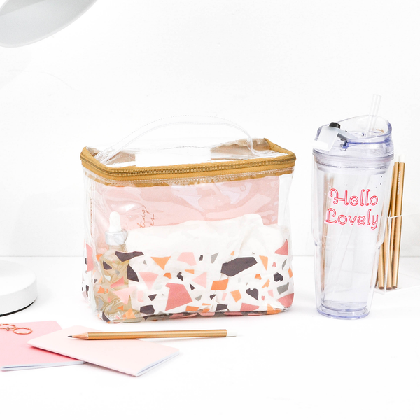 A cute toiletries bag in a terrazzo pattern surrounded by  cute desk accessories and a hello lovely clear tumbler.