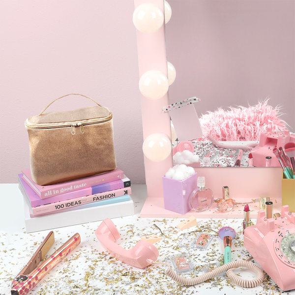Sparkly vanity with confetti, a straightener, pink retro phone, and large toiletries bag in metallic gold.