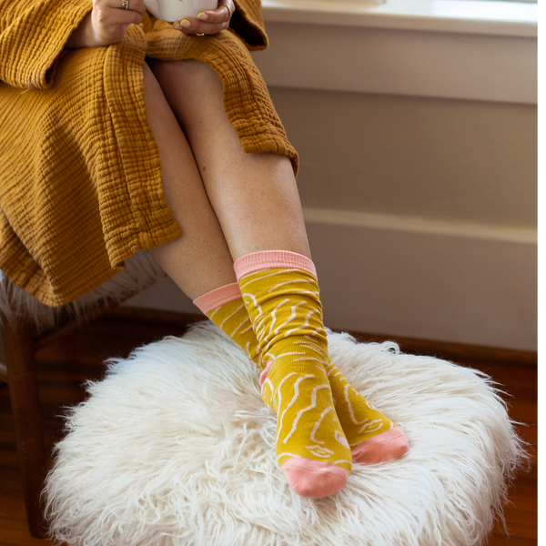 Long socks with Zen Lady design printed on the sock in white. Toes, heel, and top ankle part of the sock is in dusty pink. Socks are displayed on a person with their ankles crossed.