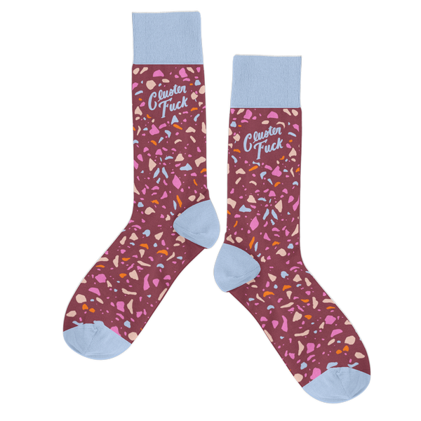 A pair of socks with a multicolored terrazzo design with a cranberry-colored background. Top part of the sock and the toe of the sock is a light blue color and the phrase "Cluster Fuck" is printed above the ankle in the same color blue.