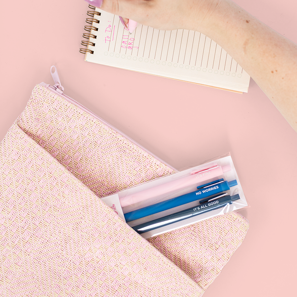 A pink and cream, cross stitch pouch with a side pocket. Doll face pouch is displayed with a set of Jotter pens, along with a lined-page task pad.
