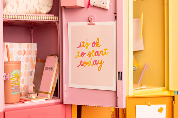 An 8x10 pink, orange, and yellow poster inside a locker that reads "it's ok to start today"