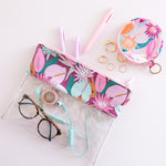 floral nights flat lay pouch with glasses, headphones and pens inside sitting on a white desk.