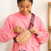 A blush pink and gold checkered cross body bag with a burgundy strap