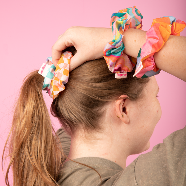 Scrunchies on a girls write while a checkered scrunchy is keeping up her ponytail.