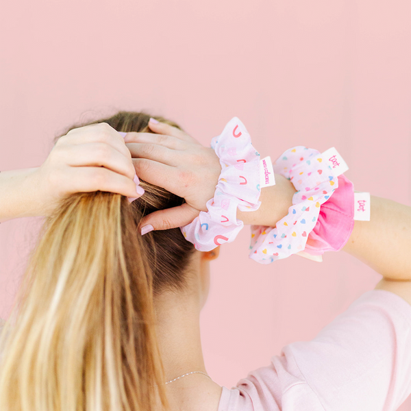 A woman putting hair up with ripstop scrunchies, one with rainbows, one with hearts, one a colorful ombre.