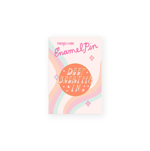 round enamel pin with orange background and pink words saying deep breaths in