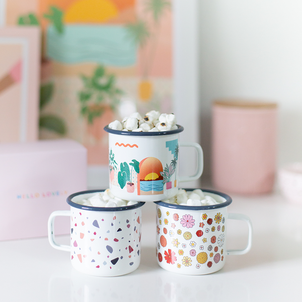 a stack of three campfire mugs one with flowers, one with a sunset and plants, and one terrazzo