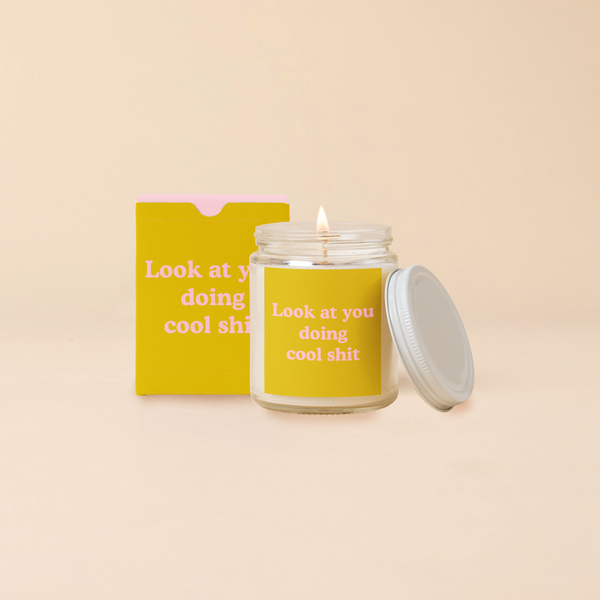 A 8 oz. candle jar with lid, with a yellow decal on it that reads "Look at you doing cool shit" printed on.