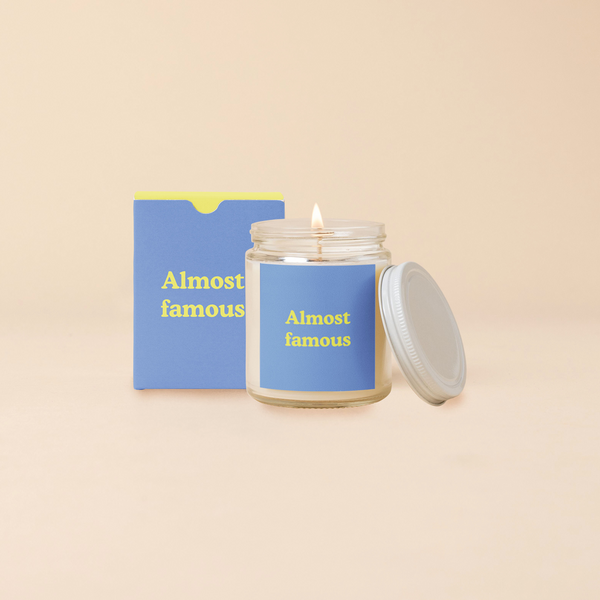A 8 oz. candle jar with lid, with a blue decal on it "Almost famous" printed on.
