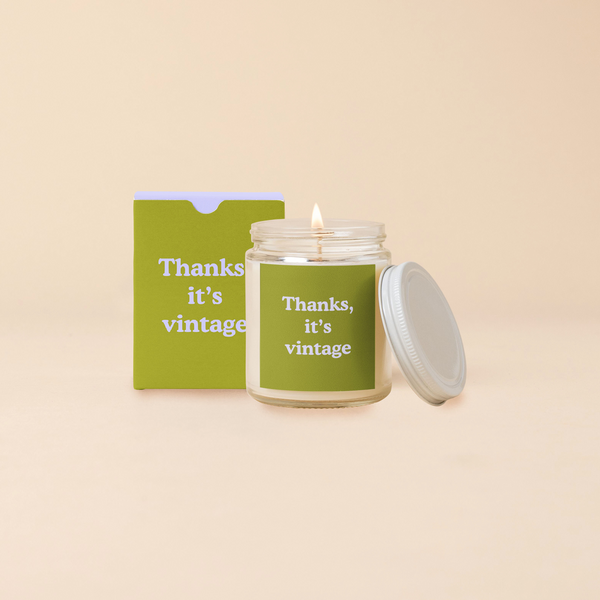 A 8 oz. candle jar with lid, with a green decal on it "Thanks, it's vintage" printed on.