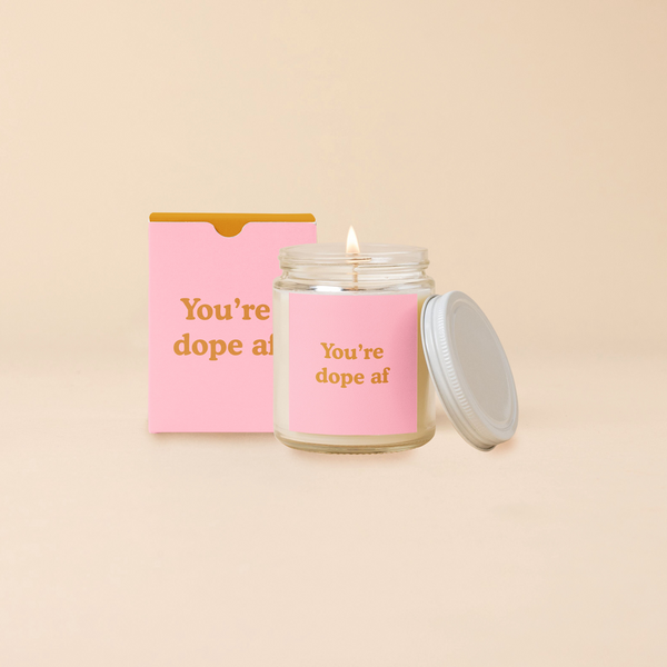A 8 oz. candle jar with lid, with a light pink decal on it "You're dope af" printed on.