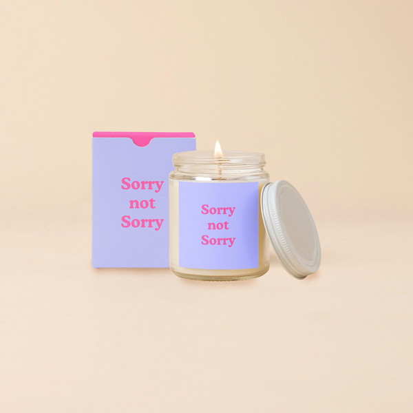 A 8 oz. candle jar with lid, with a lavender decal on it "Sorry not Sorry" printed on.