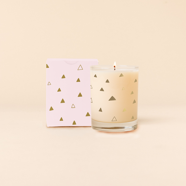 14 oz Rocks glass candle with multi-size gold triangles pattern wraps around glass. Box packaging with same pattern sits behind candle.