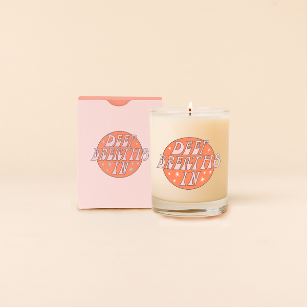 Rocks glass candle reading "DEEP BREATHS IN" in pastel pink with star backdrop. Box packaging in pastel pink with same text as candle. 