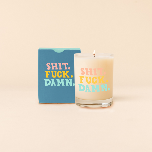 Rocks glass candle with multi-color text reading "Shit. Fuck. Damn.". Box packaging with same text as candle. 