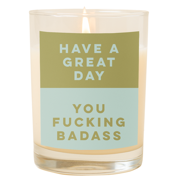 A candle with a decal that says, "Have a great day you fucking badass." The top half is an olive green color and the bottom half of the decal is a dusty blue color.